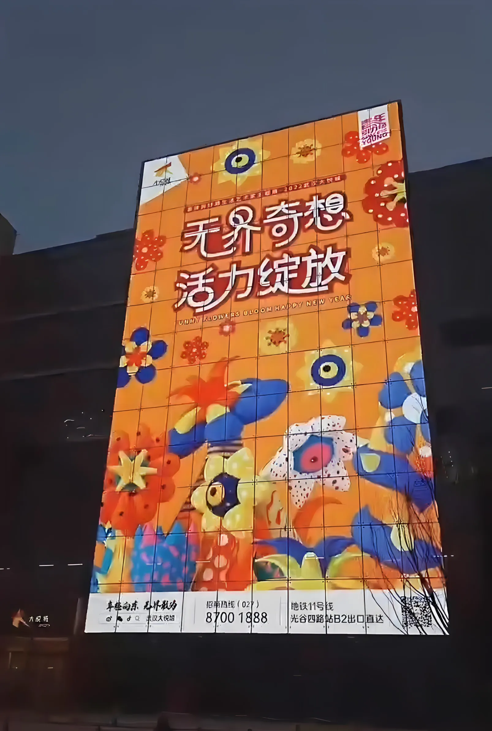 Transparent LED glass facade with colourful floral artwork at night