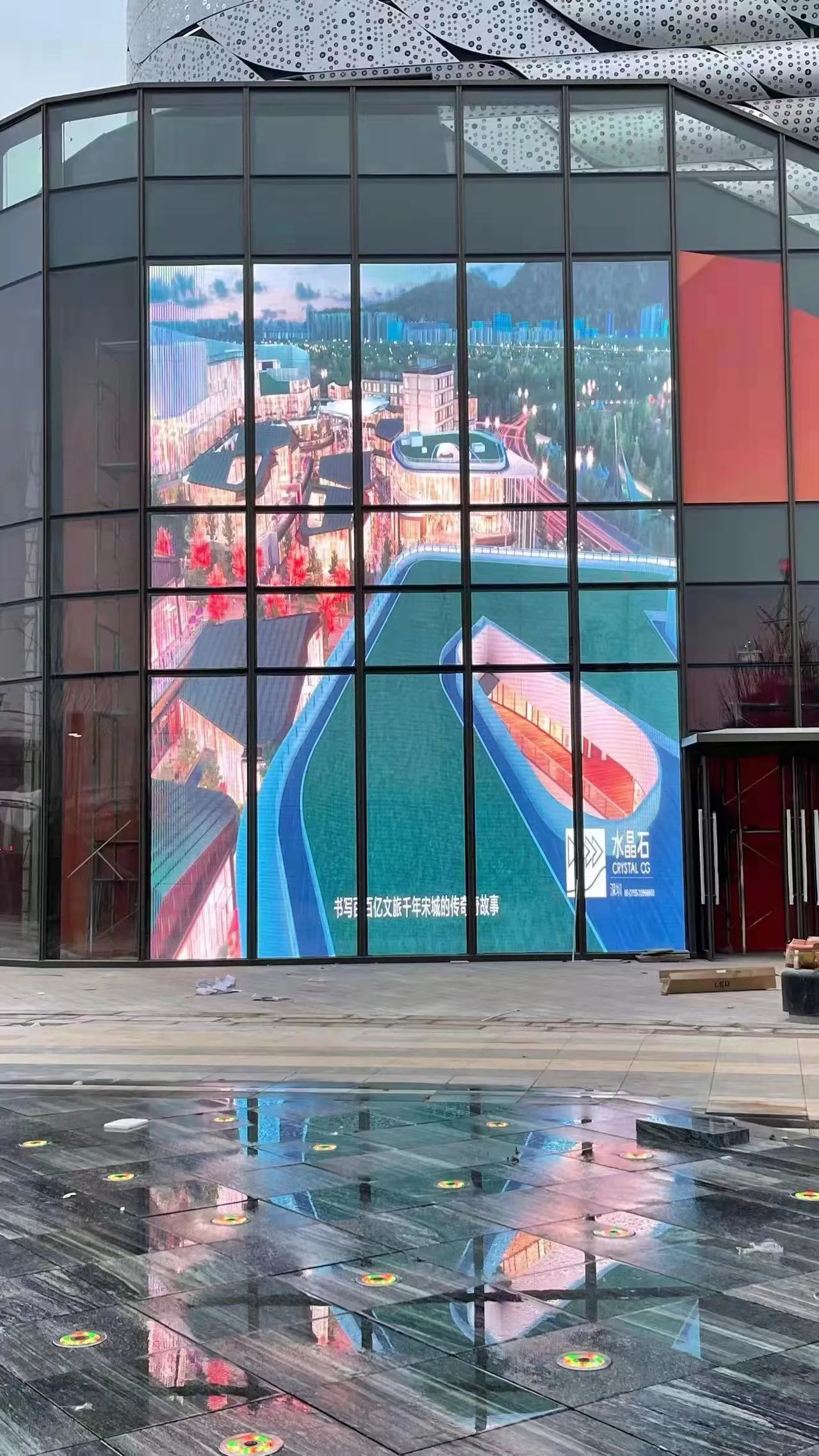 Building corner with a transparent LED glass facade showing a cityscape