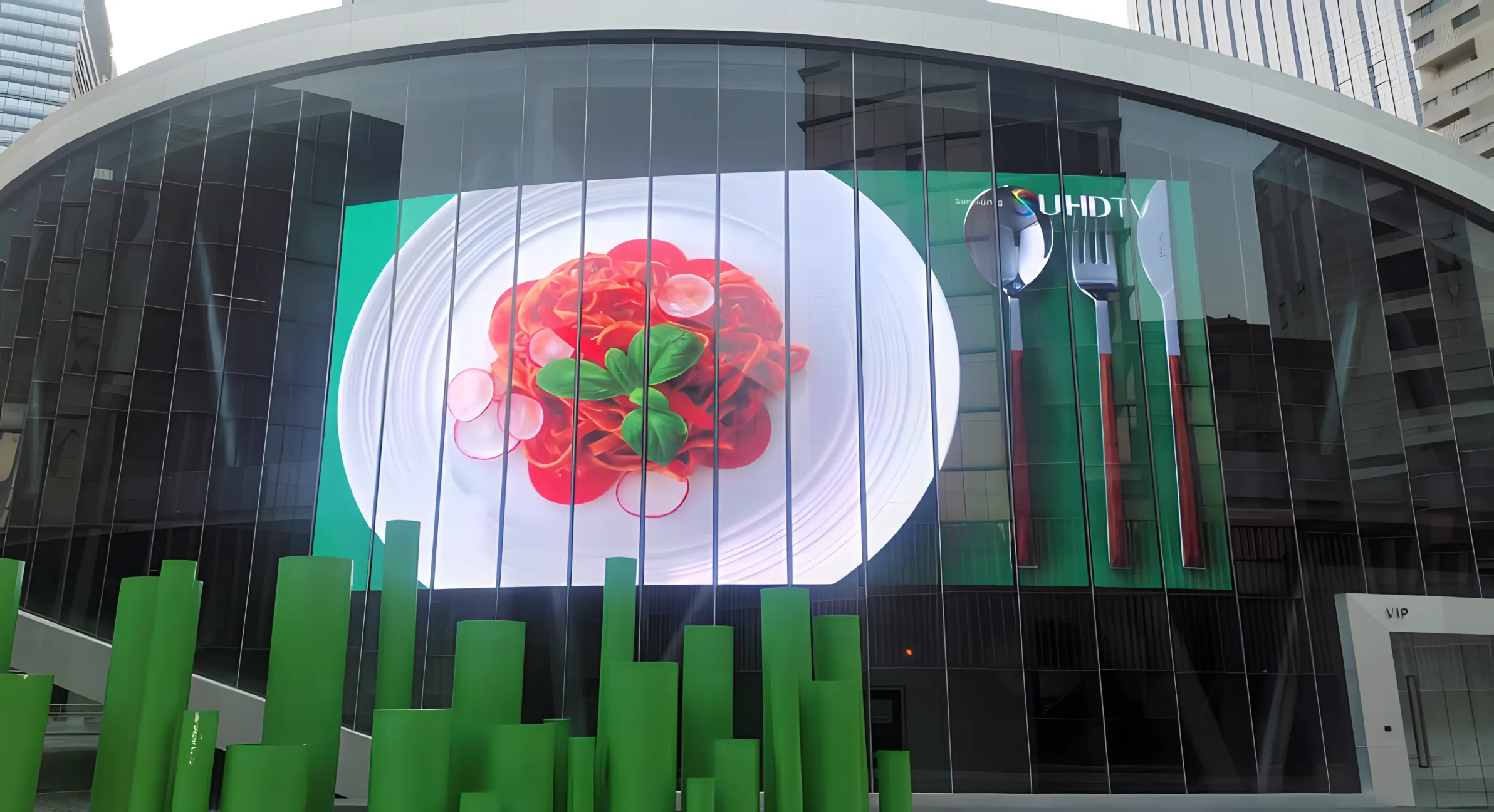 Curved glass facade glowing with green and red visuals at dusk